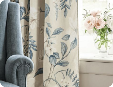 Floral curtains in cream and blue hang near a soft blue armchair.