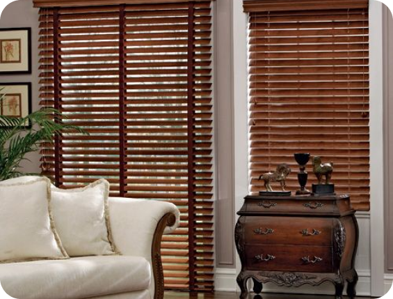A window has dark wooden blinds with light curtains and filtered sun.