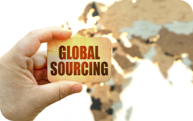 A hand holds a GLOBAL SOURCING block with a blurred world map in the background.